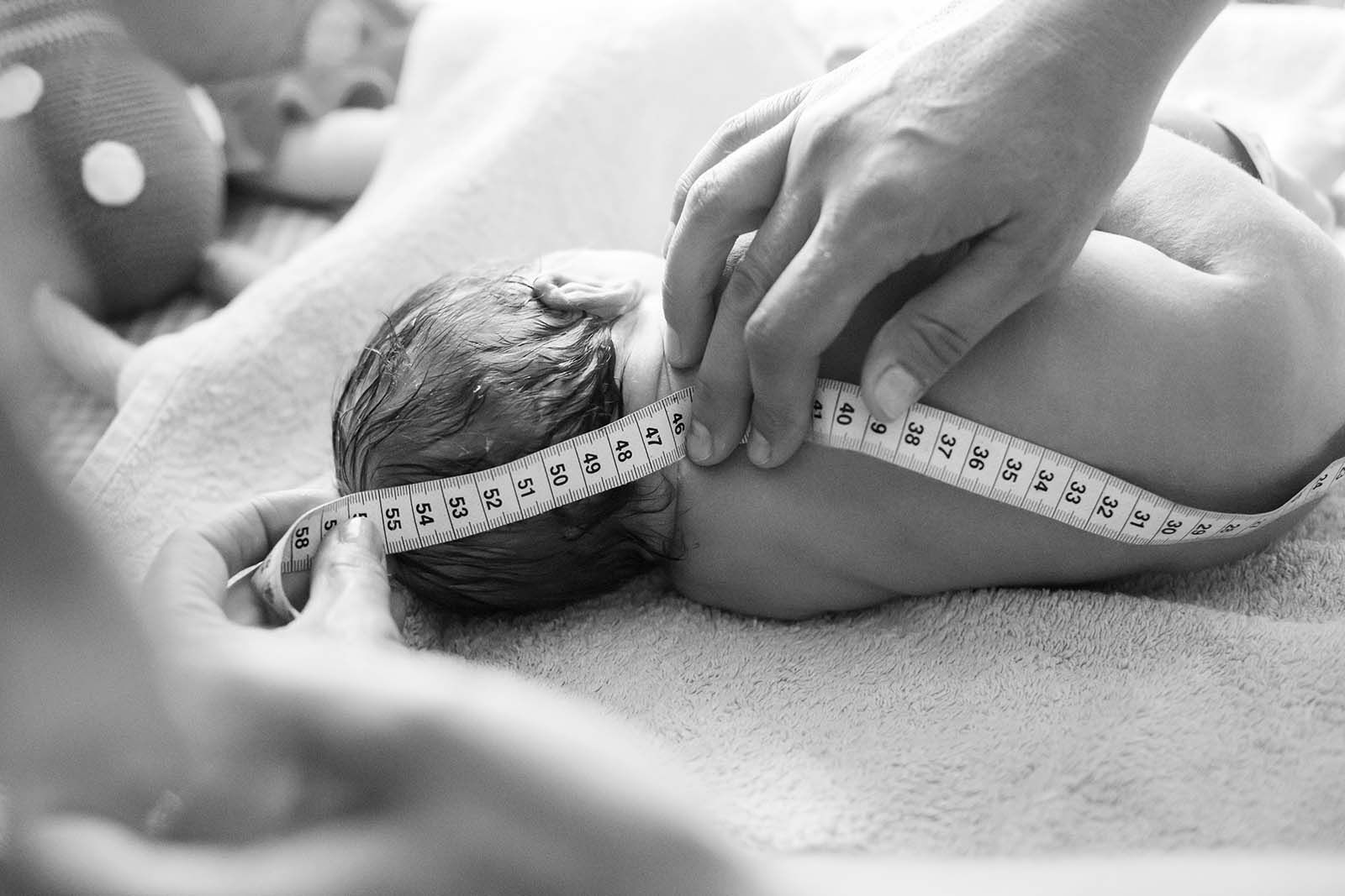 Ein Baby, welches kurz nach der Geburt mit einem Maßband vermessen wird.
